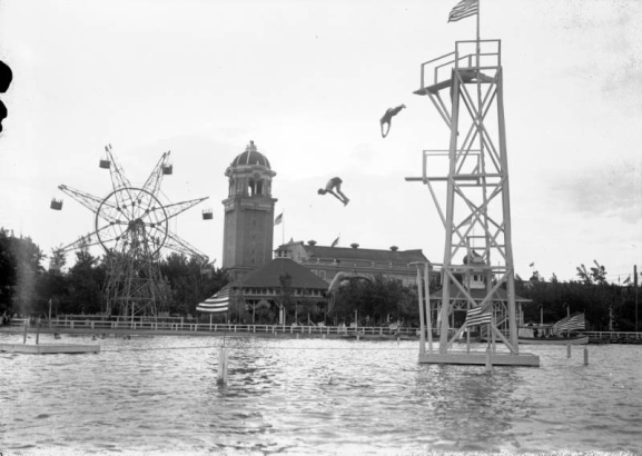 Men dive into Lake Rhoda at Lakeside Amusement Park in Lakeside (Jefferson County), Colorado; the casino tower and a ferris wheel are in the background.
