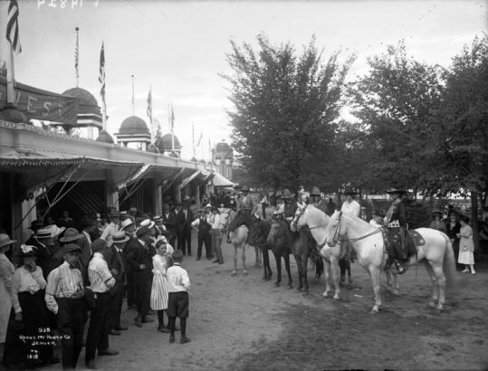 Men, women, boys, and girls look at people on horses at Lakeside Amusement Park, Lakeside (Jefferson County), Colorado.