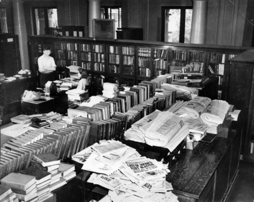 View of the Western History department in the Denver Public Library at Colfax Avenue and Bannock Street in the Civic Center neighborhood of Denver, Colorado. A man and woman stand and sit near a desk. Books and newspapers are in the room.