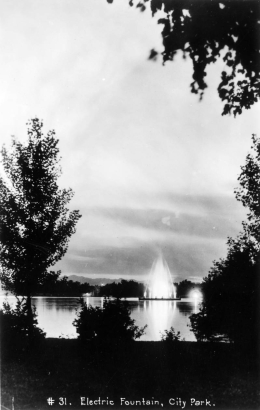 Silhouetted trees frame a view of the Electric Fountain in City Park Lake (Ferril) in Denver, Colorado. Streams of water extend high into the air and electric lights illuminate the spray.