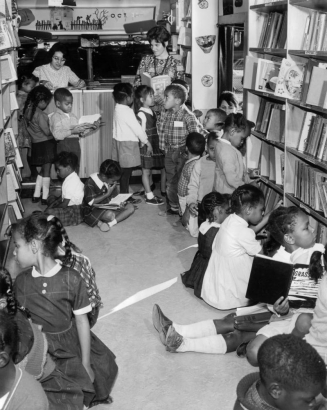 Interior view of the Denver Public Library bookmobile in Denver, Colorado; Helen V. Watts and Ellen Berner watch Black (African American) boys and girls read books.