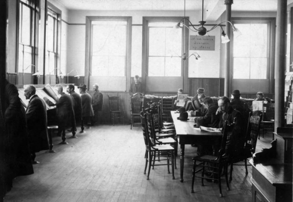 Interior view of the Denver Public Library newspaper reading room at at 15th (Fifteenth) and Court Place in downtown Denver, Colorado; one of the men is identified as M. Ritchie.