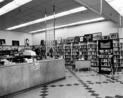 Interior view at Dahlia Branch of the Denver Public Library in Denver, Colorado; a Black (African American) man sits at the counter. Paintings top bookshelves.