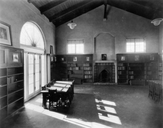 Interior view of the Elyria branch of the Denver Public Library in the Elyria-Swansea neighborhood of Denver, Colorado; decor includes open-beamed ceilings, a fireplace, book shelves, hanging lamps, French and lunette windows.