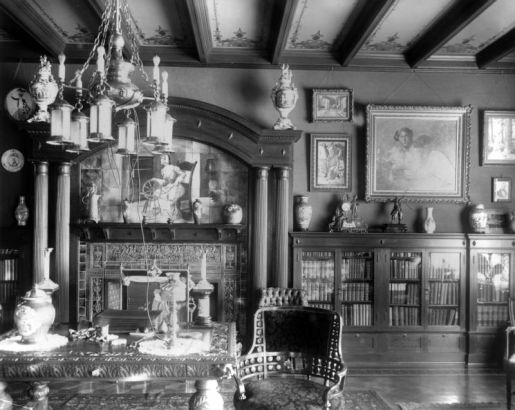 Interior view of the Alonzo Thompson residence (Baerresen Brothers Architects) in Denver, Colorado; decor includes a fireplace, carved wood columns, a chandelier, urns, bookshelves, china, framed paintings, a coffered ceiling, and stencils. A table and chair have acanthus motifs; a mosaic depicts a woman at a spinning wheel.