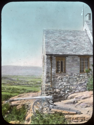 View at Charlford, near Sedalia, Douglas County, Colorado; a manor designed in 1926 for Charles Johnson by Burnham and Merrill Hoyt and built of native volcanic rock. A howitzer is by the slate roof structure.