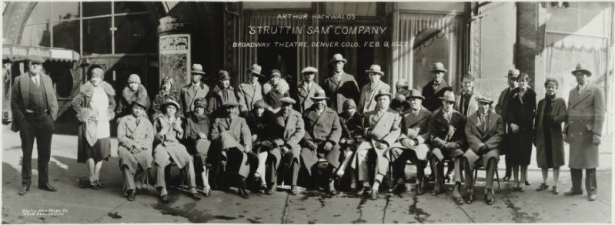 Panoramic view of the cast of Arthur Hockwold's "Struttin' Sam from Alabam'" musical company, presented at the Broadway Theater, 1756 Broadway, in Denver, Colorado. African American men and women and one white man sit and stand in front of the theater near the canopied front entrance. Sign on the canopy reads: "50 People [with] Orchestra." Sign on the window reads: "Broadway Rotisserie."