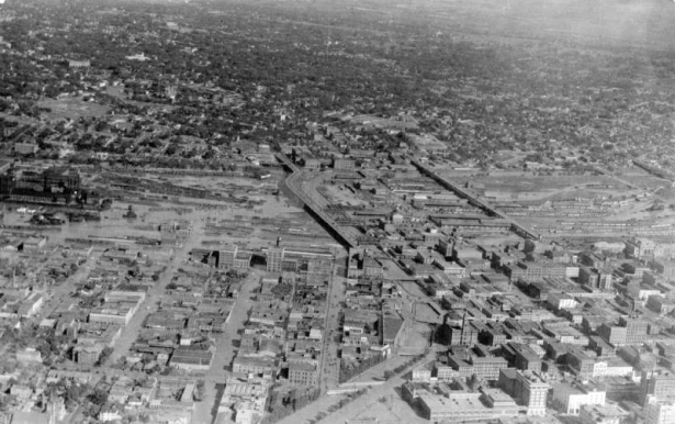 Aerial view of Cherry Creek floodwater and damage in Denver, Colorado after the Castlewood Canyon Dam break; shows the confluence of Cherry Creek and the South Platte River, railroad yards, viaducts, the Denver Tramway powerhouse, the Auraria and Highland neighborhoods, and downtown buildings including City Hall and Union Station.