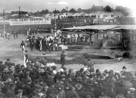 A crowd of people surrounding people barbecuing at the Denver Union Stockyard