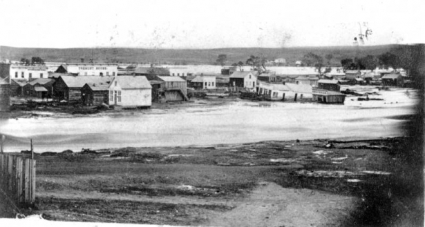 View of Denver, Colorado during a Cherry Creek flood; shows frame buildings and houses. Storefront signs read: "Tremont House" and "Groceries."