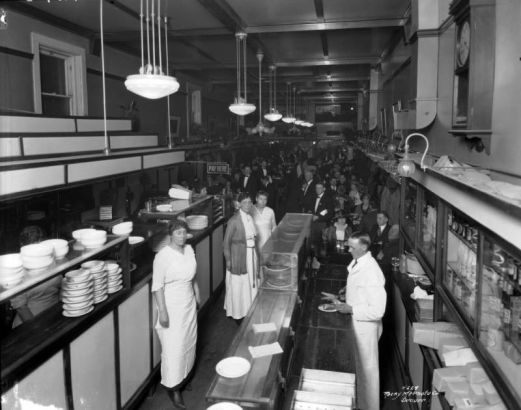 Interior view of Pell's Oyster House in Denver, Colorado; shows men, women, dishes, light fixtures, and a sign: "Pay Here."