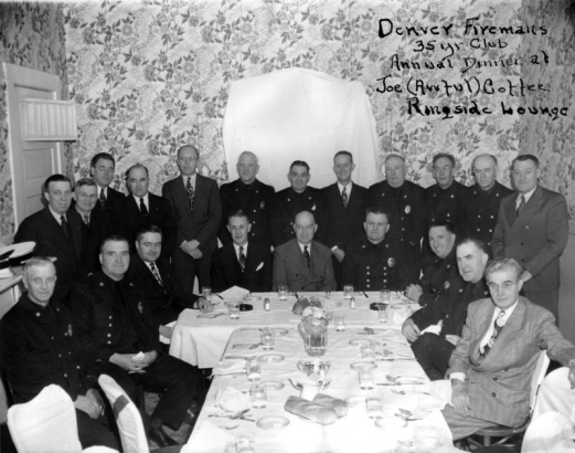 Firemen pose with dinnerware at Joe (Awful) Coffee's Ringside Lounge in Denver, Colorado. The room has floral wallpaper.