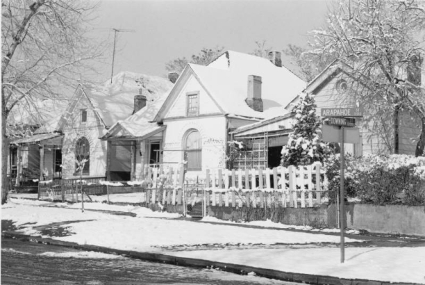 View of single family residences at the corner of Arapahoe and Downing Streets in the Five Points neighborhood of Denver, Colorado. Architectural features include chimneys, arched windows, an ocular window, decorative brick coursing and covered porches with square post and spindle supports.