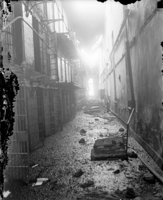 Interior pipe railed metal balconies front cell blocks at the State Penitentiary in Canon City, Colorado, after the riot of 1929. Doors are open, fire damage consists of debris and holes in the roof.
