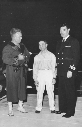 Men stand and pose in a boxing ring. Joe Rutofsky "Awful" Coffee smiles and poses between two men. Everett O. Marshall wears lace-up boxing shoes and a robe with satin lapels, cuffs, and a belt. William Harrison (Jack) Dempsey wears a military uniform with a double breasted jacket and three stripes on the sleeves.