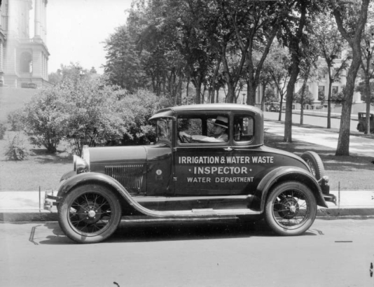 A man poses in a Water Department service truck by the Colorado State Capitol building in Denver, Colorado; lettering on the truck reads: "Irrigation & Water Waste Inspector, Water Department."