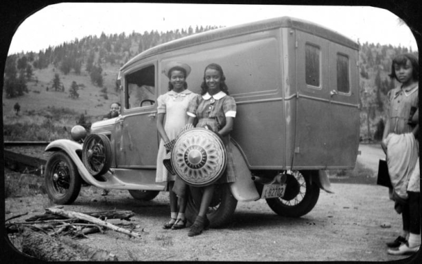 Four African American teenage campers stand by a truck at Camp Nizhoni in Lincoln Hills (Gilpin County), Colorado. One camper holds a patterned, wide-brimmed hat. The license plate on the Ford truck reads: "Colo. 1937  1-82702."