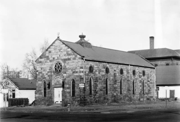 View of Congregation Shearith Israel (Emmanuel Chapel) at 10th (Tenth) and Lawrence Streets in the Auraria neighborhood of Denver, Colorado; shows an ashlar stone building with buttresses, a rosette window, and a Star of David. Hebrew letters read: "Bet Ha Knesset Shearith Yisroel." Washington School is in the background.