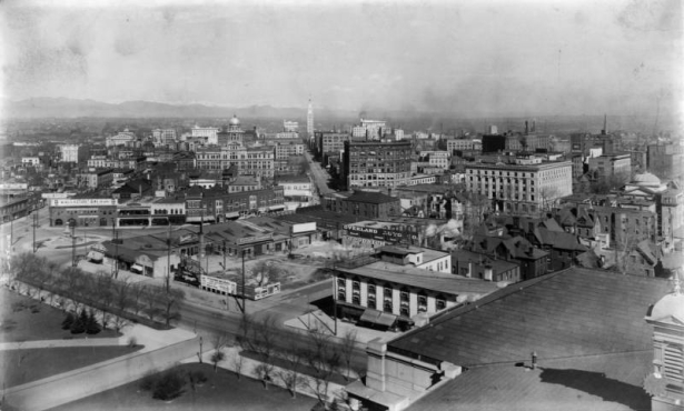 View of Denver, Colorado and snow-capped Front Range mountains. Landmarks include the Pioneer Monument; Arapahoe County Courthouse; YMCA; the Daniels and Fisher tower; and Colfax, Lincoln, and 16th (Sixteenth) Streets. Civic Center landscaping and the roof of the State Capitol are in the foreground.