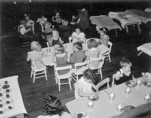 Children eat at tables in a W.P.A. nursery school in Denver, Colorado; food includes cake and tin cups of milk.