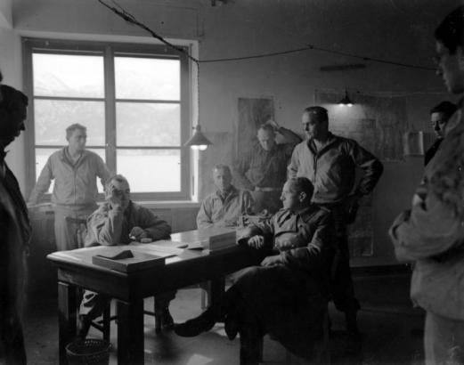 General George P. Hays (left) questions Lt. General Hildebrandt of the Marco Polo Division of the German Army (with glasses) at Tenth Mountain Division headquarters on Lake Garda, Italy, May 1945. The generals sit in Gen. Hays' office, seven soldiers look on, including his son, George J. Hays, directly behind his father, and General David L. Ruffner, Division Artillery Commander, seated to the left of Hays.