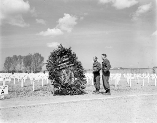 Two soldiers regard the wreath with a banner that reads: In memory of the men of the 10th Mountain Division. In the background are rows of white crosses marking the graves of Tenth Mountain Division soldiers and other servicemen buried in the American military cemetery in Castelfiorentino (Florence Province), Italy.