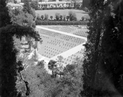 View taken from above of the American Military Cemetery, where many Tenth Mountain Division soldiers are buried, in Castelfiorentino, Italy. Shows rows of white crosses surrounded by trees.