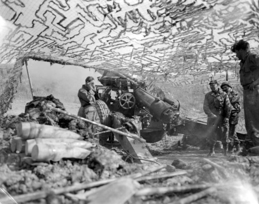 Four soldiers, from a unit in support of the Tenth Mountain Divisin Infantry, fire heavy artillery from beneath a camouflage.