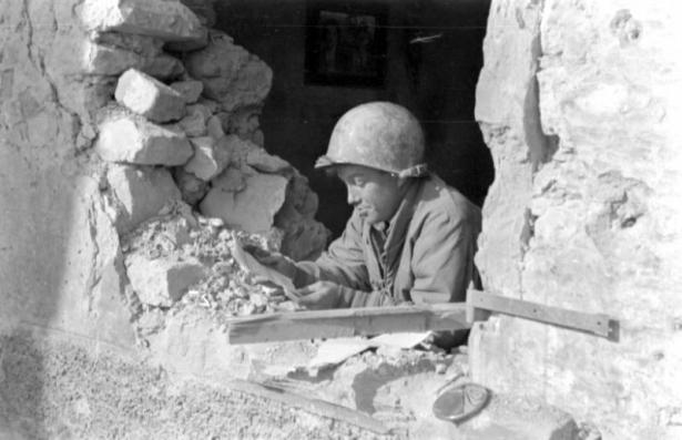 Casmer Omilian of the Tenth Mountain Division, 87th Regiment, Company I, reads a letter from home in the window of a rubble-strewn and artillery-shattered stone building.