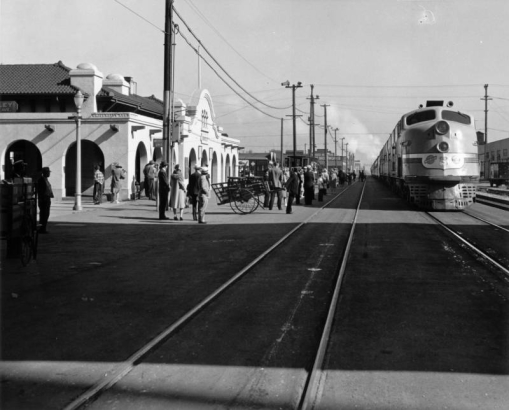 View of the Southern Pacific Railroad depot on University Avenue in Berkeley (Alameda County), California. People walk between the Mission Style building arcades and a Chicago & Northwestern / Union Pacific locomotive and train, the "City of San Francisco."