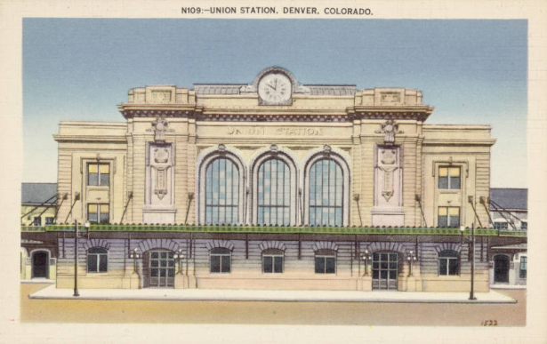 View of Union Station on 17th (Seventeenth) Street and Wynkoop Street in Denver, Colorado. The stone, classical building has a central clock, arched windows, a flat roof and a covered sidewalk.