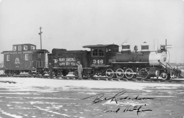 Bob Richardson and Carl Helfin wear fake moustaches and pose in front of a "Merry Christmas and Happy New Year" sign on a Denver and Rio Grande Western Railroad coal tender car in Alamosa (Alamosa County), Colorado. Shows locomotive number "346" and a caboose that reads: "Mount Blanca and Western" and "Thru the Chico." Snow is on the ground near the train.