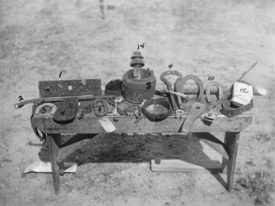 View of artifacts found at Fort Caspar in Casper (Natrona County), Wyoming. Shows harness and farrier's tools including a fish plate (from a freighter wagon), a hame and short tug, an axe, a coupling iron, a spoon, a glue pot, a yoke iron, part of a musket, a bolster iron, a telegraph insulator, a wagon hub, and horse, mule and oxen shoes.