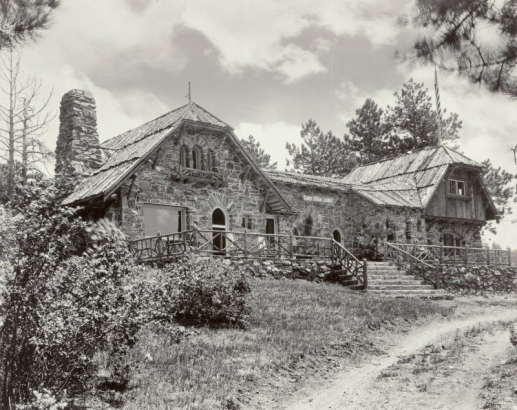 View of Chief Hosa Lodge, built beside the (onetime) Denver to San Francisco stagecoach road, in Genesee Mountain Park (Denver Mountain Parks), Jefferson County, Colorado. The rustic inn, designed by architect Jacques Benedict, is made of "Rainbow" granite and lodge-pole pine, and features hipped gables, timber siding, a deck, steps, arched doors and windows.