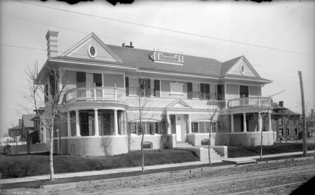 A round porch stands on each end of the large residence of Judge Henry T. Rogers at 1739 East 13th (Thirteenth) Avenue in Denver, Colorado. Shutters hang from the windows on the house. Columns support the portico. A round window on the front door has "1739" painted on it.