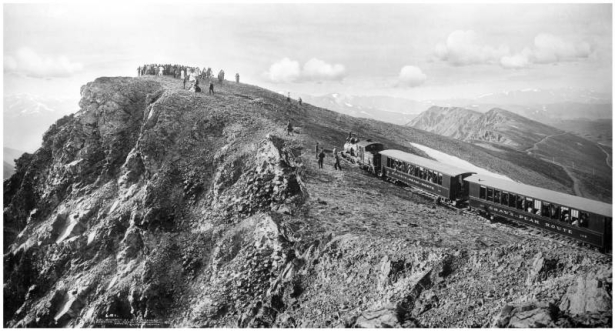 Mount McClellan's summit (14,007 feet) via Argentine Central Railway, Colorado; shows engine and passenger cars parked with large group of sightseers at summit and in cars, passenger cars retouched to reflect name of "Gray's Peak Route," narrow gauge track, and Rocky Mountains in background.