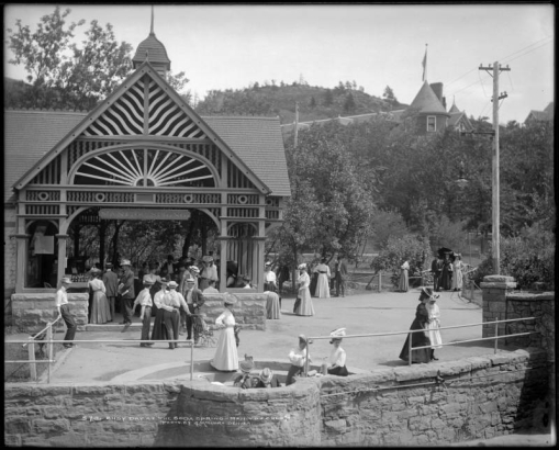 Manitou Springs, Colorado, trolley stop (Colorado Springs and Interurban Railway) with Soda Springs drinking fountain, center foreground; shows men and women fashionably attired gathered around springs and trolley  shelter, and Cliff House Hotel, one block from Soda Springs.