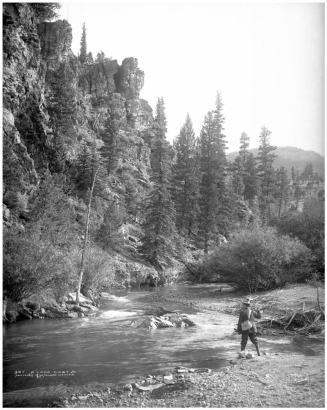 One man fishing in South Platte River in Platte Canyon possibly near Glenisle, Colorado, reached via Colorado and Southern Railway; fisherman casting into stream with wicker creel on shoulder.