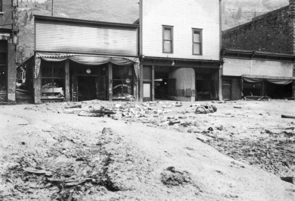View north towards businesses on Colorado Avenue after the Cornet Creek flood on July 27, 1914, Telluride, Colorado. Mud and debris fill street in front of three false front wood frame structures between Sheridan Hotel and First National Bank, including the Phoenix Market.