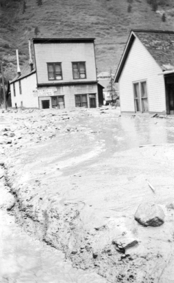 View north up mud and debris-filled street from the disastrous Cornet Creek flood on July 27, 1914, Telluride, Colorado; shows two-story false front, Iowa House on corner, and residence across street.