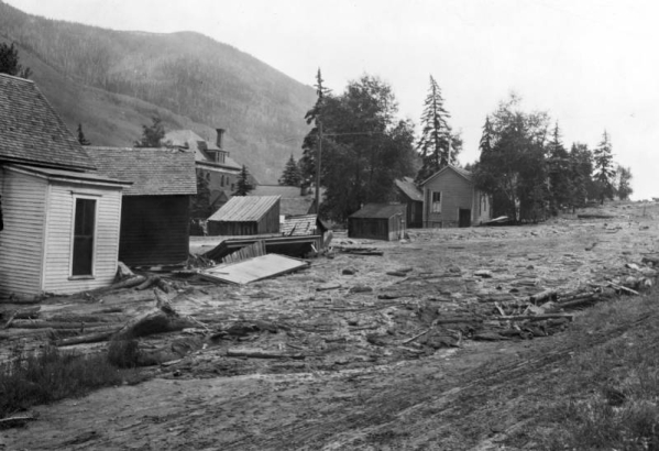 Street scene after the Cornet Creek flood on July 27, 1914, Telluride, Colorado. Mud and debris fill street with damaged wood-frame structures; Miner's Union Headquarters and Hospital are in background.