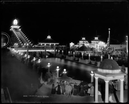 The White City, later called Lakeside Amusement Park, during a summer evening, Lakeside, Colorado near Denver; night time view of amusement park area with illuminated rides, sidewalks and buildings, people at ticket gazebo, the Big Splash, Casino Theater and Cafe.