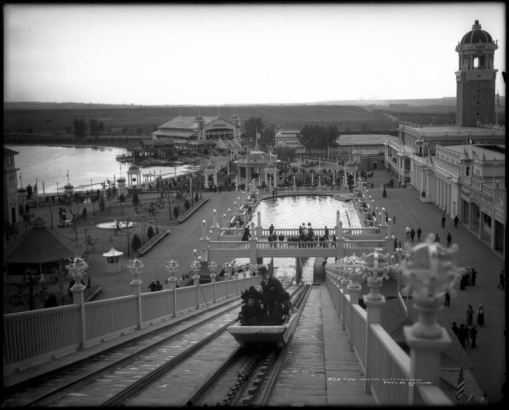 View of the "White City" (later called Lakeside Amusement Park), Lakeside, Colorado near Denver; northern view over park area taken from the Big Splash ride shows people in car on water ride, others standing on deck, main entrance with tower and casino, bandstand or pavilion (gazebo) with benches, Lake Rhoda, miniature train tracks, ball room, boat house, and rink.