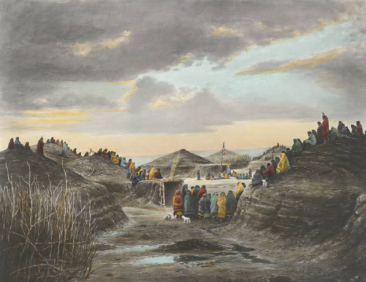 North American Indian (Pawnee) men and women sit and stand on and near earthen lodges at sunset probably in Nebraska. They are wrapped in blankets. Shows fences made of twigs or brush, and a plaza with an American flag that flies near the entrance to a lodge.