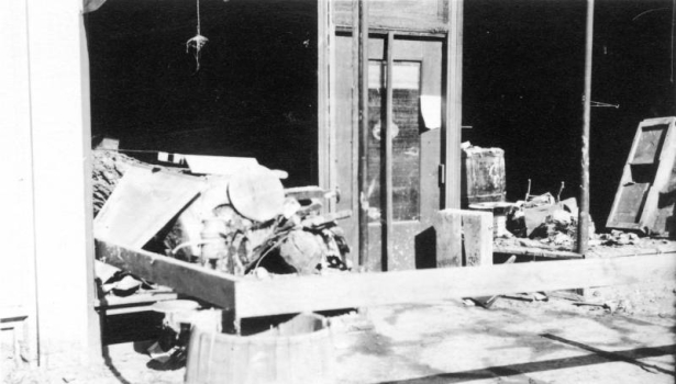 The trunk of a cottonwood tree and debris are pushed through the display window of the Pierce Seed Company at 216 W 4th (Fourth) Street after an Arkansas River flood in Pueblo, Colorado. Part of the wall and the window frame have collapsed.
