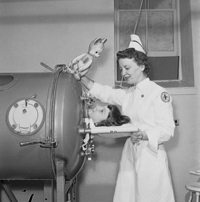 A Red Cross nurse talks to a woman in an iron lung (respirator) at Denver General Hospital (Denver Health Medical Center) in Denver, Colorado. Her uniform has a patch that reads: "American Red Cross," and she holds a toy stuffed rabbit.