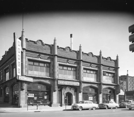View of James Motor Company at 1278 Lincoln Street (at 13th / Thirteenth) in Denver, Colorado; features include stone gothic arches, stepped pediments with shield motifs and spindles. Signs read: "Dodge," "Plymouth," and "Parts."