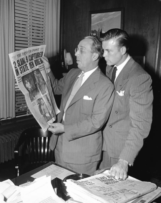 Scott Brady, star of "Canon City," and Palmer Hoyt, editor and publisher of the Denver Post from 1946-1971, with a Denver Post newspaper, look at the headlines in an office in Denver, Colorado. A sheet with "The Denver Post Deadline Schedule" sits on the desk. The headline, about the 1947 prison break on which "Canon City" was based, reads: "2 Slain, 9 Captured, In State Pen Break, Stir Crazy Cons Lead Pen Break."