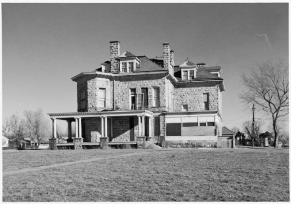 View of an abandoned house at 2305 South Washington Street in the Rosedale Neighborhood of Denver, Colorado. The ashlar stone home has chimneys, covered and enclosed porches, and a faceted turret.