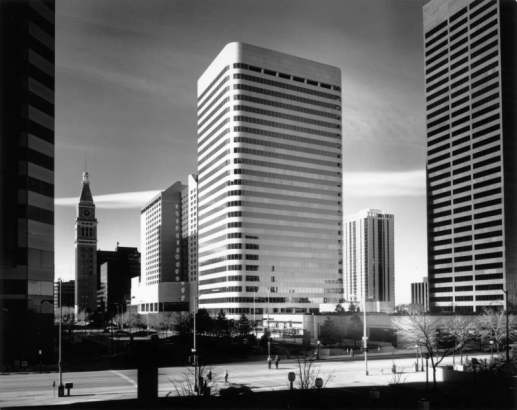 View of downtown Denver, Colorado; shows the Westin Hotel (with light reflections), the May D & F clock tower, and Larimer Place Condominiums. Office buildings include Denver National Bank (round corners). Pedestrians walk on 17th (Seventeenth) Street; the Central Bank Building is in the distance.